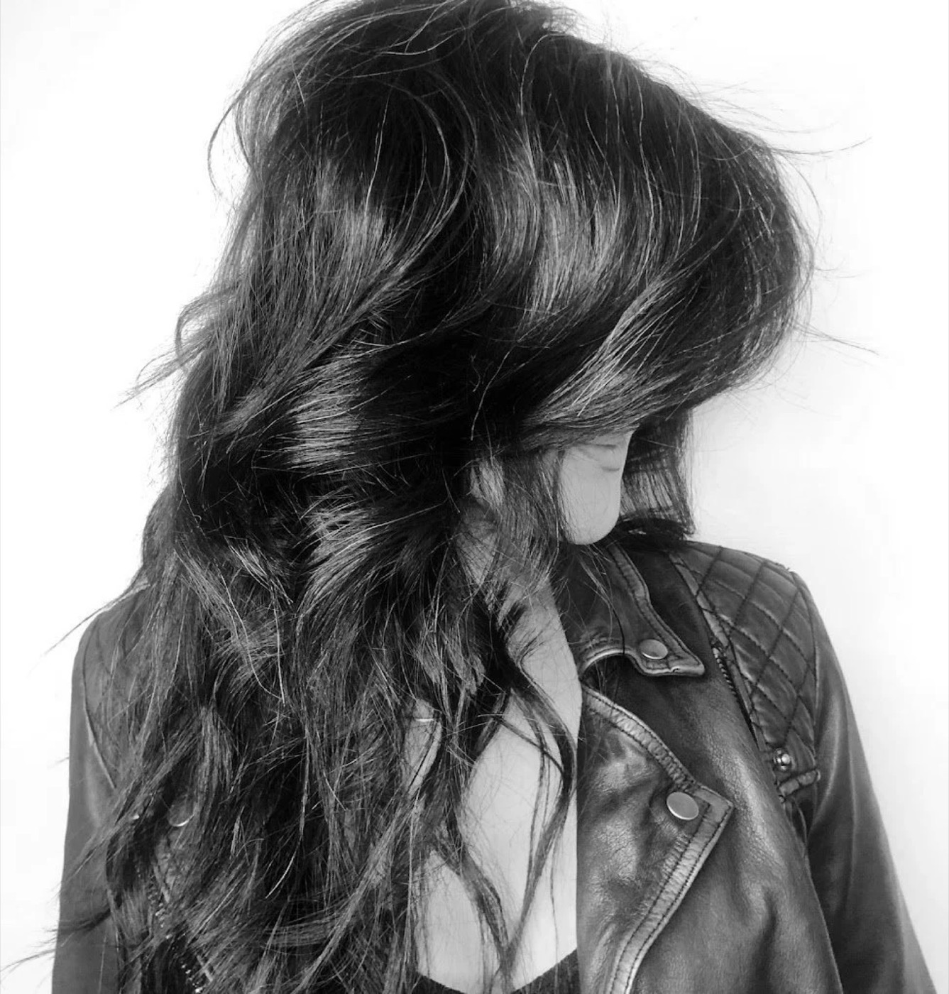 A woman with long, wavy hair wearing a leather jacket, looking down.